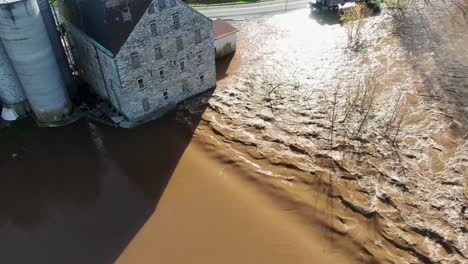 Aerial-of-stone-mill-flooded-by-hurricane,-muddy-Conestoga-River-in-Lancaster,-PA,-USA