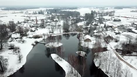 Scenic-smooth-Bird's-eye-view-over-calm-village-by-frosted-lake-at-winter