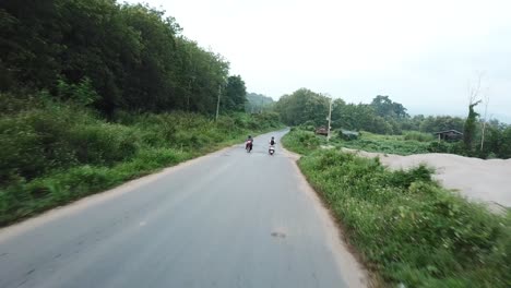 Tracking-Aerial-View-of-Authentic-Laos-Countryside-Road-and-Motobike-Scooter-Riders-on-Gloomy-Morning