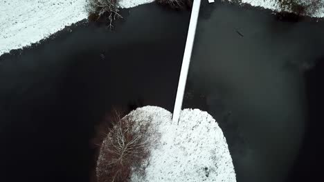 Luftaufnahme-Von-Oben-Nach-Unten-Auf-Einer-Kleinen-Schneebedeckten-Brücke-Von-Einer-Kargen-Insel-Auf-Einem-Zugefrorenen-See