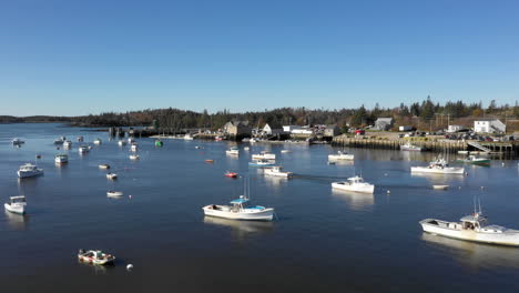Aerial-Fly-Over-Drone-Footage-of-boat-leaving-harbor-flanked-by-parked-boats,-Maine-Coast,-Vinalhaven,-Fox-Islands,-Knox-County,-Maine,-USA