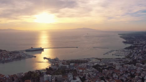 Aerial-drone-slow-motion-Flight-over-mitilini-revealing-sunrise-at-sea-with-ferry-to-athens,-lesvos,-greece