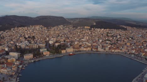 Aerial-drone-Flight-over-downtown-mitilini-revealing-sunrise-at-sea-with-ferry-to-athens,-lesvos,-greece