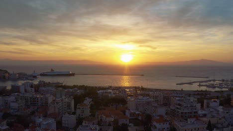 Aerial-drone-Flight-over-downtown-mitilini-revealing-golden-sunrise-at-sea-with-ferry-to-athens,-lesvos,-greece