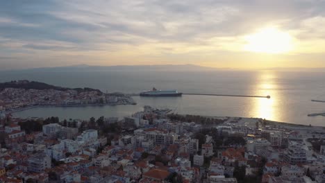 Drone-Flight-over-downtown-mitilini-revealing-sunrise-at-sea-with-ferry-to-athens,-lesvos,-greece