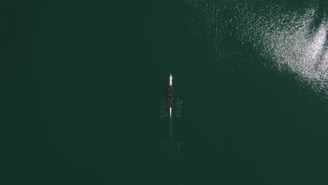 Overhead-aerial-view-of-rowing-team-in-boat-rowing-together-in-green-open-water