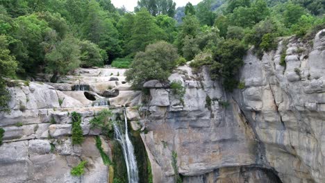 Close-to-pull-back-reveal-aerial-view-of-rocky-cliff-edge-waterfall-cascading-down-rocky-steep-drop