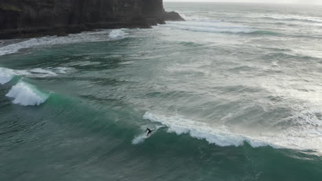 Man-catches-wave-and-surf-near-Piha-beach,-Auckland,-New-Zealand,-aerial-shot