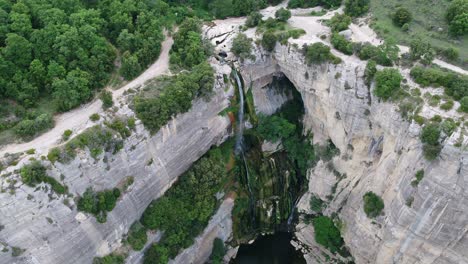 Aerial-view-above-rocky-cliff-edge-waterfall-cascading-into-water-below