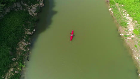 Lone-Kayak-paddles-down-river-in-Kosovo,-Aerial-rise-shot