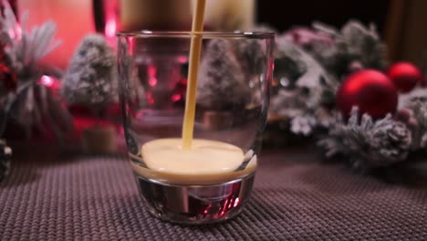 Slow-motion-push-in-of-holiday-drink-eggnog-being-poured-into-a-glass-surrounded-by-Christmas-decorations