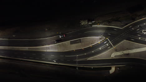 Aerial-top-down-view-traffic-crossing-illuminated-Canadian-twisting-highway-at-night