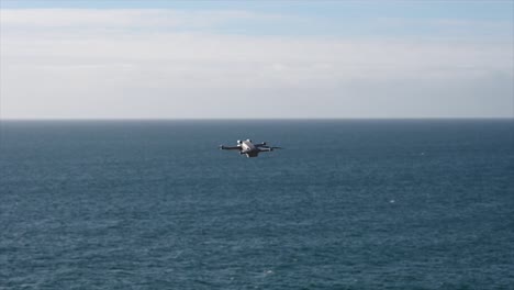 grey-drone-is-flying-over-the-sea,-propellers-turning-fast,-filmmaking-gear