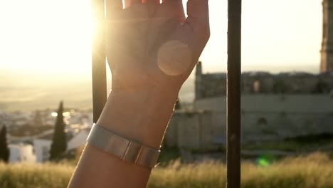 tilting-shot-of-a-model-arm-holding-onto-a-fence-with-a-church-in-the-background-during-sunset