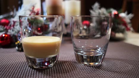 Popular-holiday-drink-eggnog-being-poured-into-two-glasses-garnished-with-Christmas-decorations
