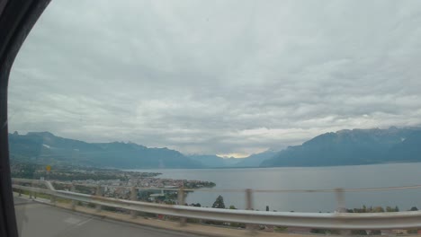 A-view-of-a-beautiful-town-underneath-the-motorway-adjacent-the-sea-and-landscape-view-of-mountains-series,-in-a-cloudy-weather,-from-the-car-window