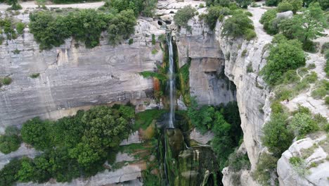 Aerial-view-pull-back-away-from-rocky-cliff-edge-waterfall-cascading-down-steep-drop