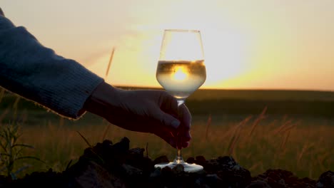 A-human-hand-picking-a-glass-full-of-white-wine-reflecting-the-sunset-and-the-sky