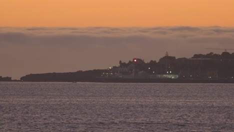 Beautiful-night-sunset-with-big-orange-sky-and-dark-clouds-with-lighthouse-giving-light-in-cascais
