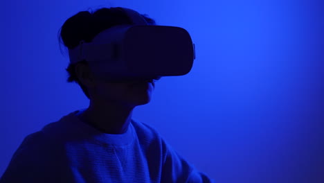 Young-teenager-wearing-VR-augmented-reality-goggles-dancing-in-blue-room