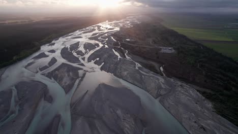 flying-over-the-Waimakariri-braided-river-towards-the-sunset-with-light-rays-in-Christchurch,-New-Zealand