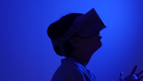 Amazed-teenager-wearing-VR-metaverse-goggles-overwhelmed-with-technology-in-blue-room