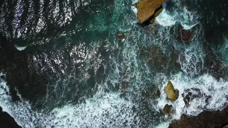 Aerial-top-down-shot-of-waves-from-ocean-crashing-against-coral-rocks-in-Indonesia