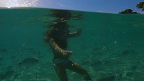 Under-water-footage-of-a-cute-little-redhead-girl-with-diving-mask-surrounded-by-school-of-fish-feeding-them-with-bread