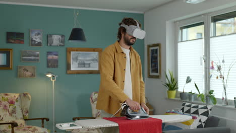 Middle-aged-adult-male-ironing-clothes-wearing-virtual-reality-goggles-tech-in-modern-home