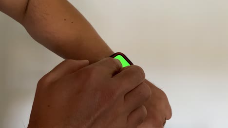 Young-male-person-wearing-fitness-bracelet-with-green-screen-close-up