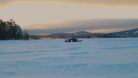 Tractor-travelling-across-snowy-Norbotten-landscape-preparing-Lapland-ice-lake-track-during-early-morning-sunrise