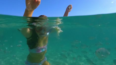Underwater-scene-of-a-cute-little-girl-with-diving-mask-surrounded-by-school-of-fish-feeding-them-with-bread