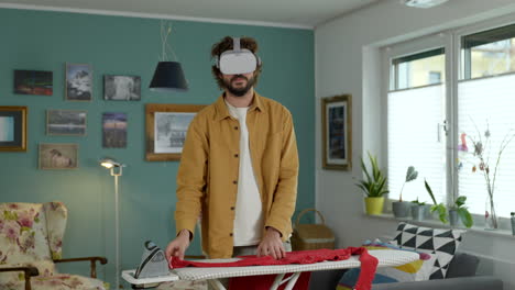Young-adult-man-ironing-clothes-wearing-virtual-reality-goggles-tech-in-modern-home