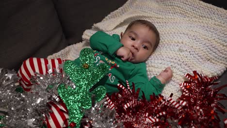 Adorable-2-Month-Asian-Baby-Boy-Lying-On-Blanket-Wearing-Festive-Christmas-Outfit-Sucking-On-Left-Hand-With-Red-And-Silver-Tinsel-Beside-Him