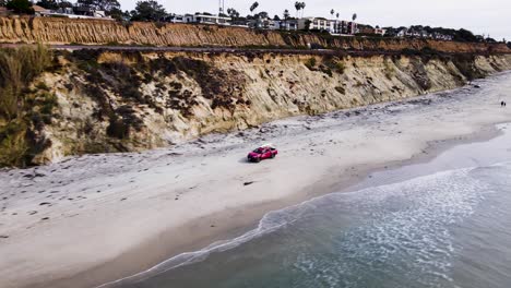 Aerial-view-of-a-red-lifeguard-truck-driving-on-the-beach-near-the-cliffs-in-Delmar