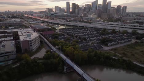 Train-in-front-of-I-69-and-the-Houston-skyline,-dusk-in-Texas,-USA---Aerial-view