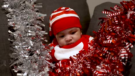 Entzückender-2-Monate-Alter-Junge-Mit-Rotem-Weihnachtsoutfit-Und-Hut,-Umgeben-Von-Rotem-Und-Silbernem-Lametta