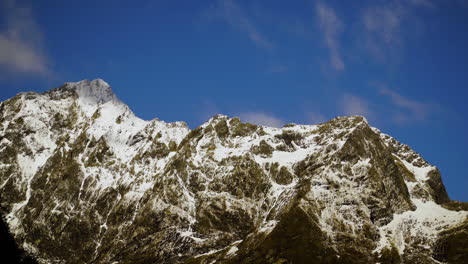 Time-Lapse-snow-capped-mountain-peaks-as-white-clouds-are-blown-across-a-blue-sky