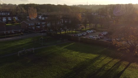 Long-sunset-autumn-shadows-across-British-neighbourhood-school-soccer-field-aerial-view