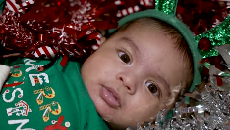 Young-Adorable-Two-Month-Old-baby-with-festive-outfit-and-Christmas-decorations-wearing-shirt-that-says-"Merry-Christmas"-Wearing-Green-Reindeer-Headband