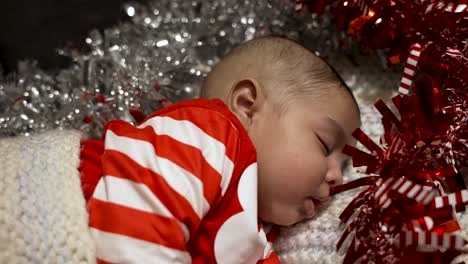 Adorable-Cute-2-Month-Old-Indian-Baby-Boy-In-Festive-Outfit-Sleeping-Surrounded-By-Red-And-Silver-Tinsel-Christmas-Decorations