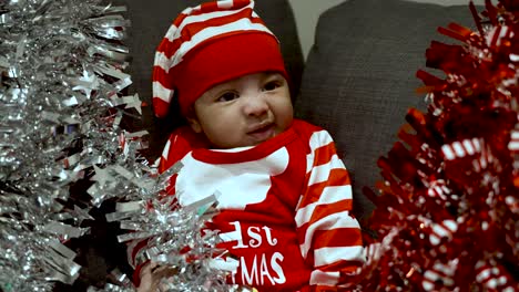Entzückender-2-Monate-Alter-Junge,-Der-Rotes-Weihnachtsoutfit-Und-Hut-Trug-Und-An-Rotem-Und-Silbernem-Lametta-Zog,-Umgab-Ihn-Auf-Dem-Sofa