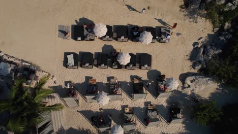 Aerial-top-down-shot-of-people-relaxing-on-sandy-private-beach-with-bay-in-sunlight---Mexico,-Tulum---ascending-straight-down-view