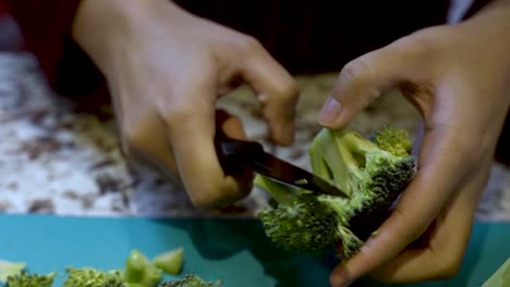 Hands-Of-Young-Asian-Woman-Carefully-Slicing-Broccoli-Over-Cutting-Board