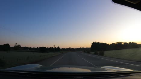 Car-Driving-On-Asphalt-Road-Through-Rural-Fields-At-Sunset