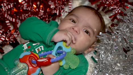 Adorable-2-Month-Bangladeshi-Baby-Boy-Lying-On-Blanket-Sucking-On-Teething-Toy-Surrounded-By-Red-And-Silver-Tinsel
