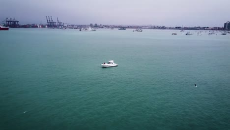 White-Boat-Anchored-Peacefully-In-Calm-Blue-Water-,-Port-In-Background,-Callao,-Peru