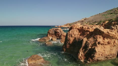 Aerial-dolly-shot-of-a-seashore-with-beautiful-red-coloured-rocks-and-turquoise-waters-of-the-Mediterranean-Sea,-Ramla-Beach-on-the-island-of-Gozo,-Malta