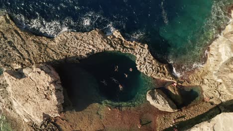 Vista-Aérea-De-Personas-Nadando-En-Un-Mar-Azul-Prístino-En-El-Famoso-Agujero-Azul-En-Dwerja-En-La-Isla-De-Gozo,-Malta