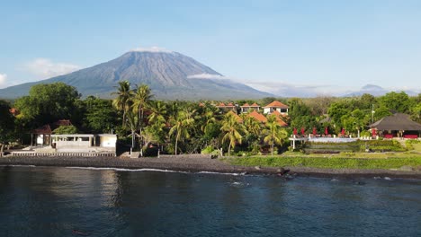 Schwenkende-Drohnenansicht-Des-Beeindruckenden-Vulkans-Mount-Agung,-Der-Sich-über-Der-Küstenstadt-Tulamben-Bali-Erhebt